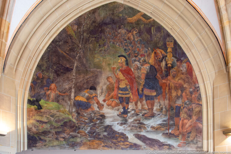 Large arched mural with armored and robed figures gathered near a rocky stream in Aachen Town Hall.