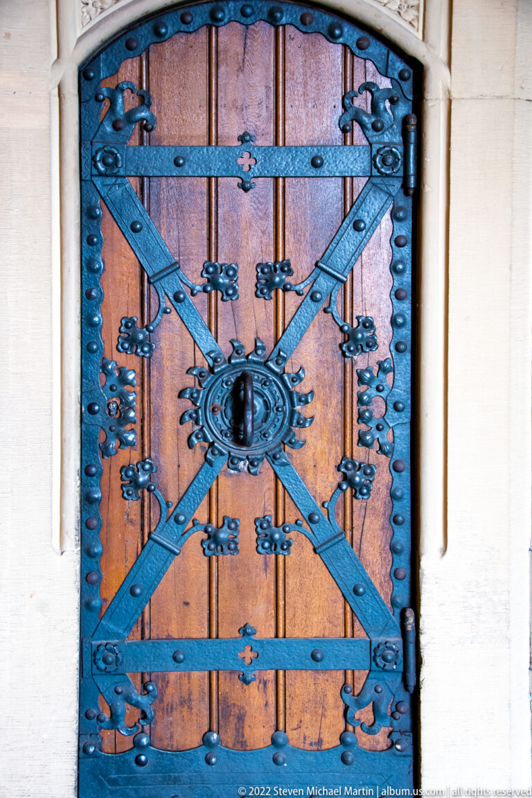 Wooden plank door reinforced with black iron straps, studs, hinges, and a circular central fitting.