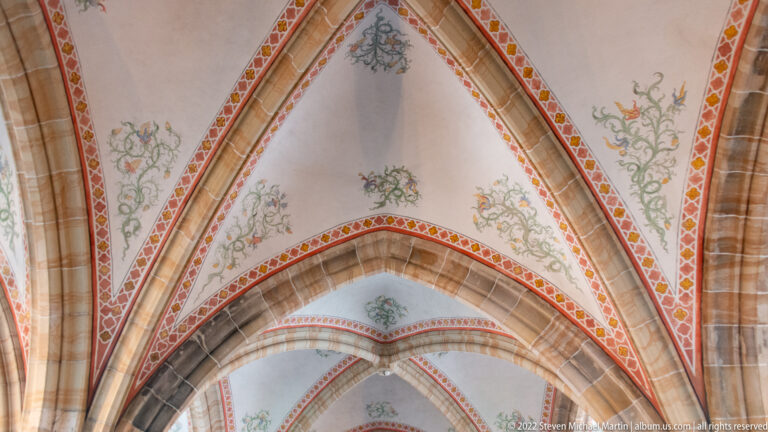 Pointed rib vaults painted with floral motifs and red-and-gold borders between stone ribs.