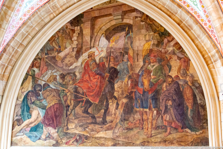 Large arched mural crowded with armed figures, fallen bodies, horses, and richly dressed participants.