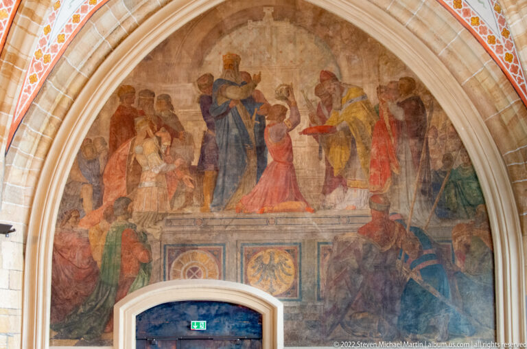 Arched mural above a doorway showing two groups of richly dressed figures in a ceremonial encounter.