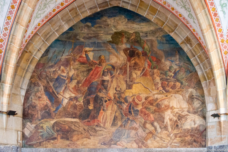 Large arched battlefield mural with fallen horses and soldiers in the foreground and fighting figures behind.