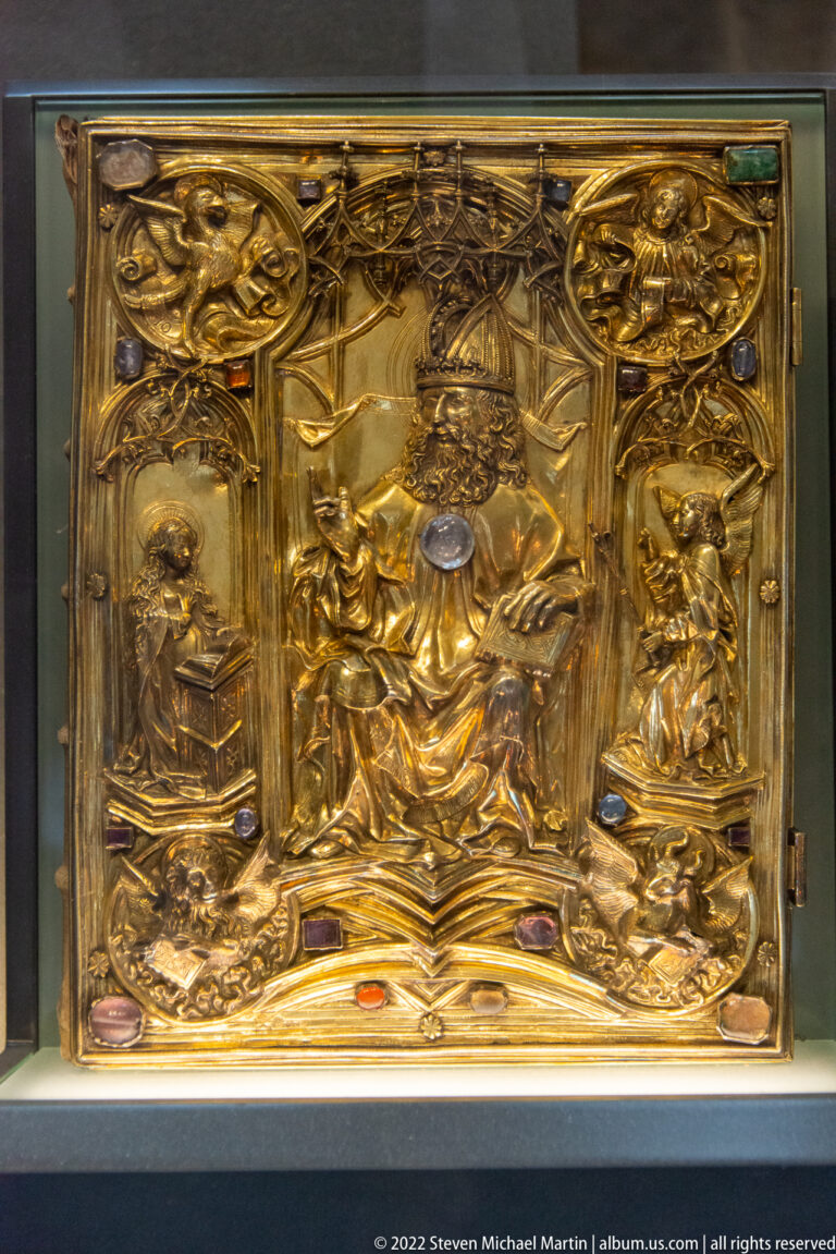 Rectangular gilded treasury object with relief figures, architectural frames, and inset colored stones.