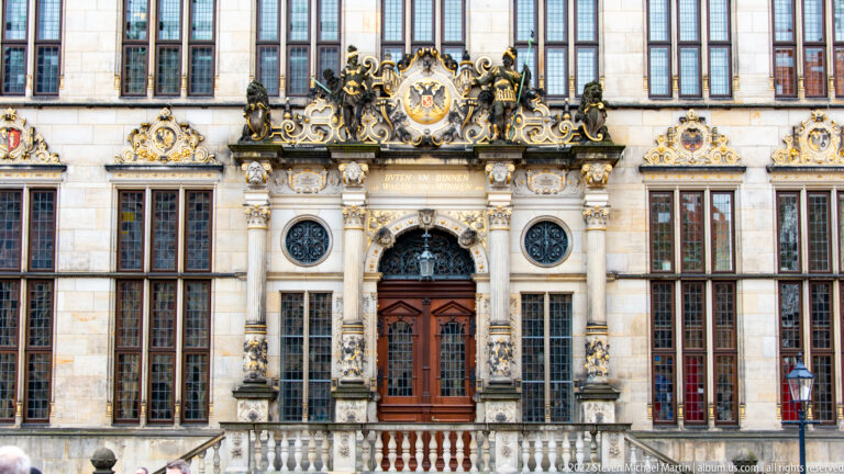 Ornate main entrance of Bremen Town Hall with carved columns, heraldic sculpture, circular grilles, and wooden doors.