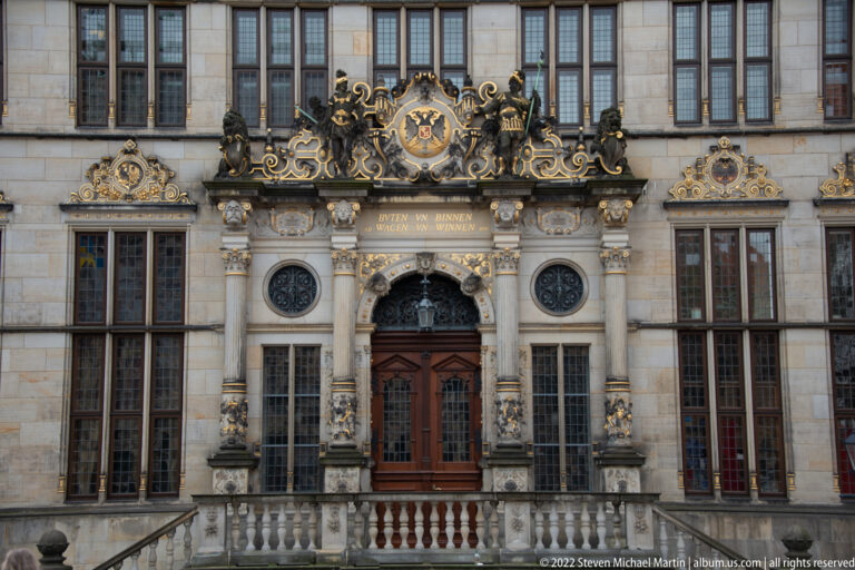 Symmetrical close view of Bremen Town Hall’s main doorway, flanking windows, round grilles, carved columns, and crest.