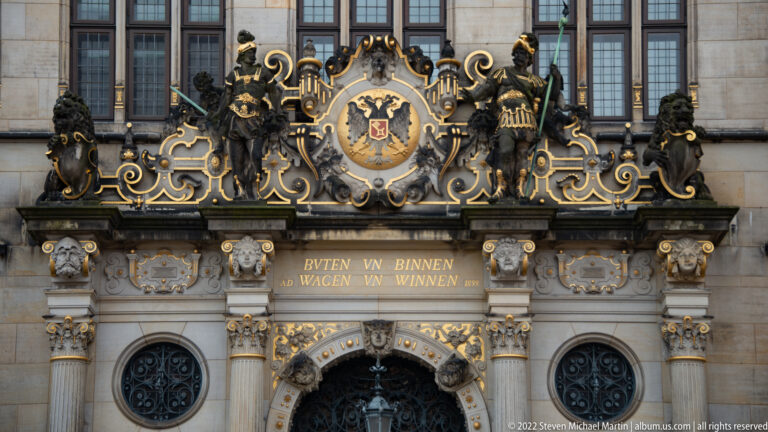 Close view of gilded heraldic crest with standing figures and animal supporters above Bremen Town Hall’s entrance.
