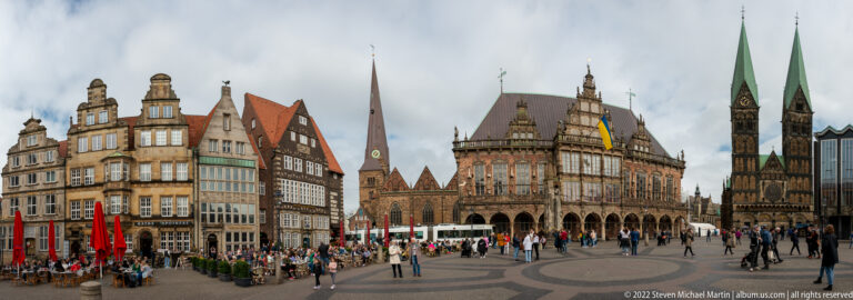 Wide market-square panorama with historic façades, Bremen Town Hall, St. Peter’s Cathedral towers, and pedestrians.