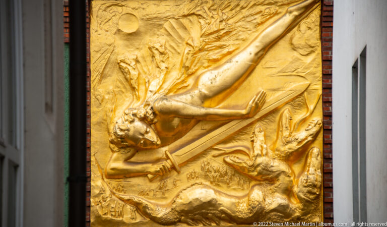 Gilded relief of a dramatic elongated figure above a writhing creature at the entrance to Böttcherstraße.