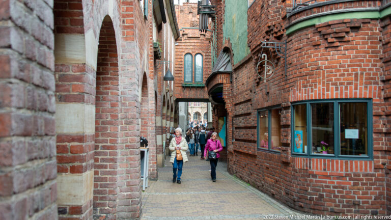 Narrow pedestrian passage between curved red-brick buildings in Bremen’s Böttcherstraße, with pedestrians and shop windows.