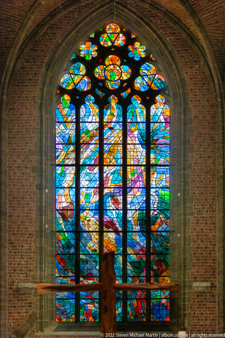 Large multi-light abstract stained-glass window glowing against dark brick and stone inside Bremen’s Church of Our Lady.