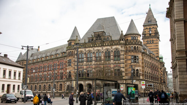 Large historic civic building with brick-and-stone façade, turrets, tall tower, and central arched entrance.