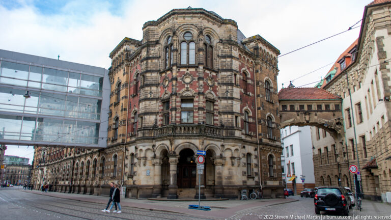 Ornate historic corner building with rounded bay, arcaded ground floor, striped stonework, and carved window surrounds.
