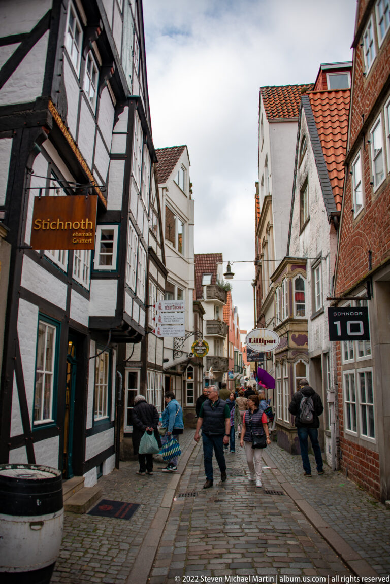 Cobblestone pedestrian street in Bremen’s Schnoor Quarter with half-timbered houses, shops, hanging signs, and pedestrians.