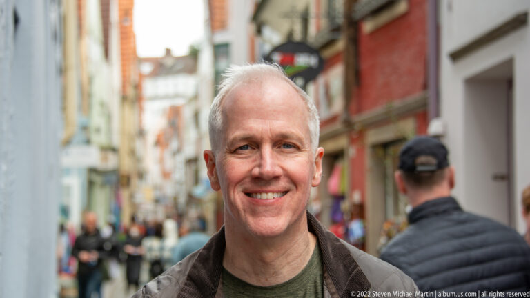 Smiling gray-haired man in a green shirt standing on a narrow historic pedestrian street in Bremen.