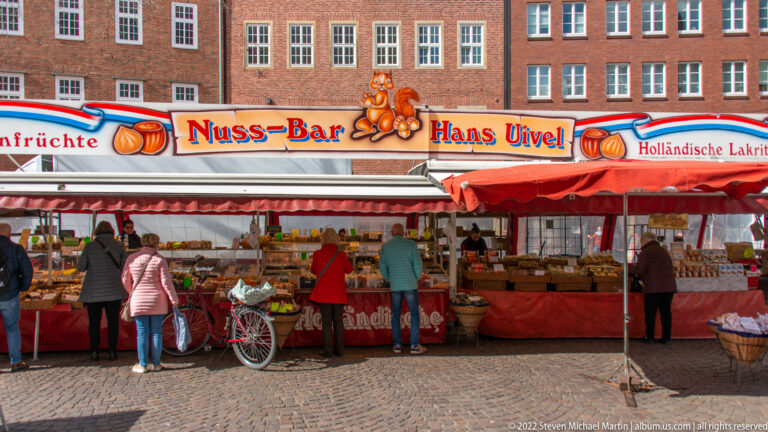 Red-and-white market stall selling nuts and Dutch licorice, with shoppers and bicycles in Bremen’s historic center.