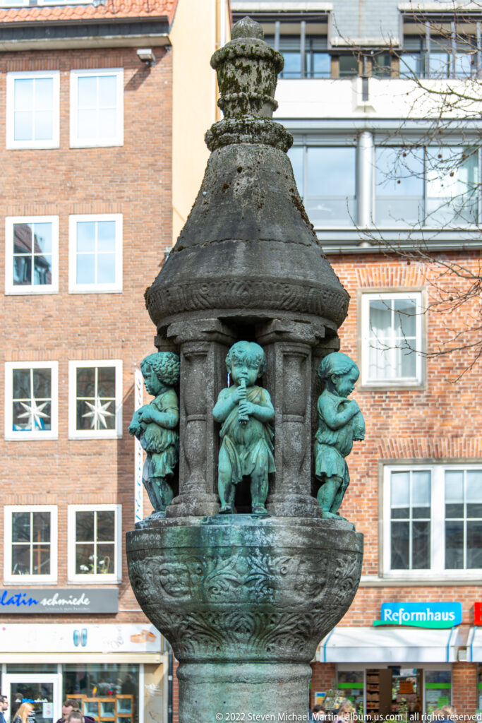 Small urban fountain with green-patinated animal figures grouped around a dark central structure.
