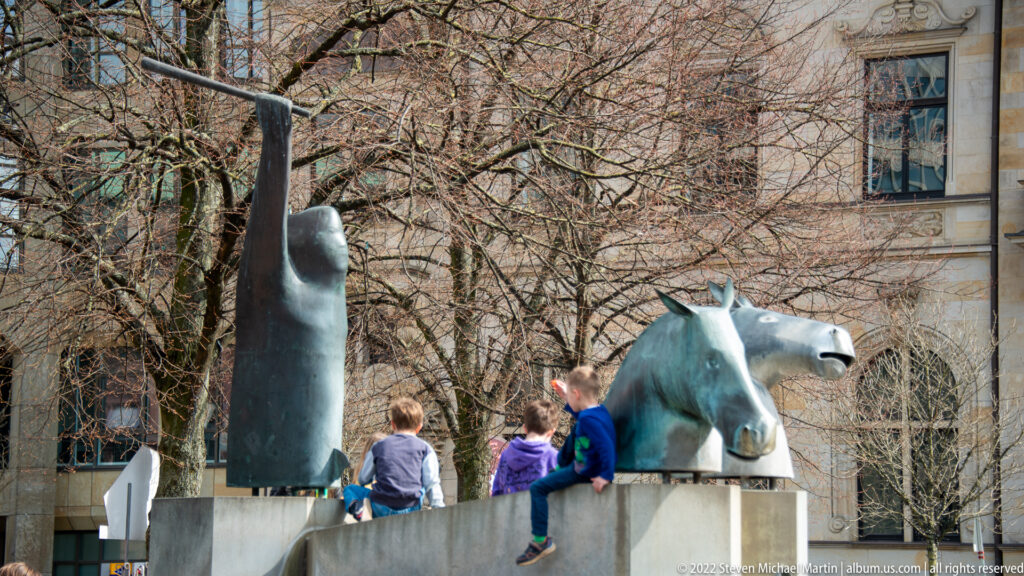 Children sitting beside a stylized metal horse sculpture on a low wall in central Bremen.