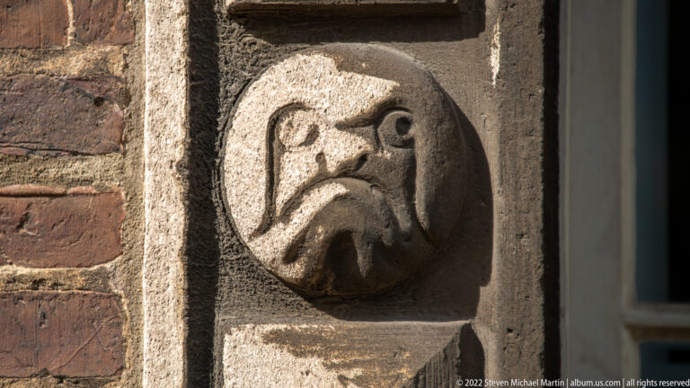 Weathered grotesque face carved in a circular stone boss set into historic masonry.