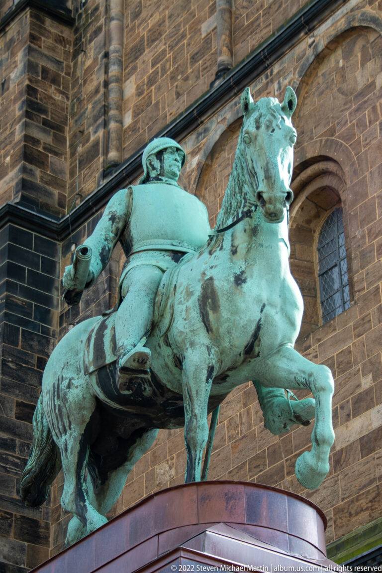 Green-patinated bronze equestrian statue of Otto von Bismarck beside the stone wall of Bremen Cathedral.