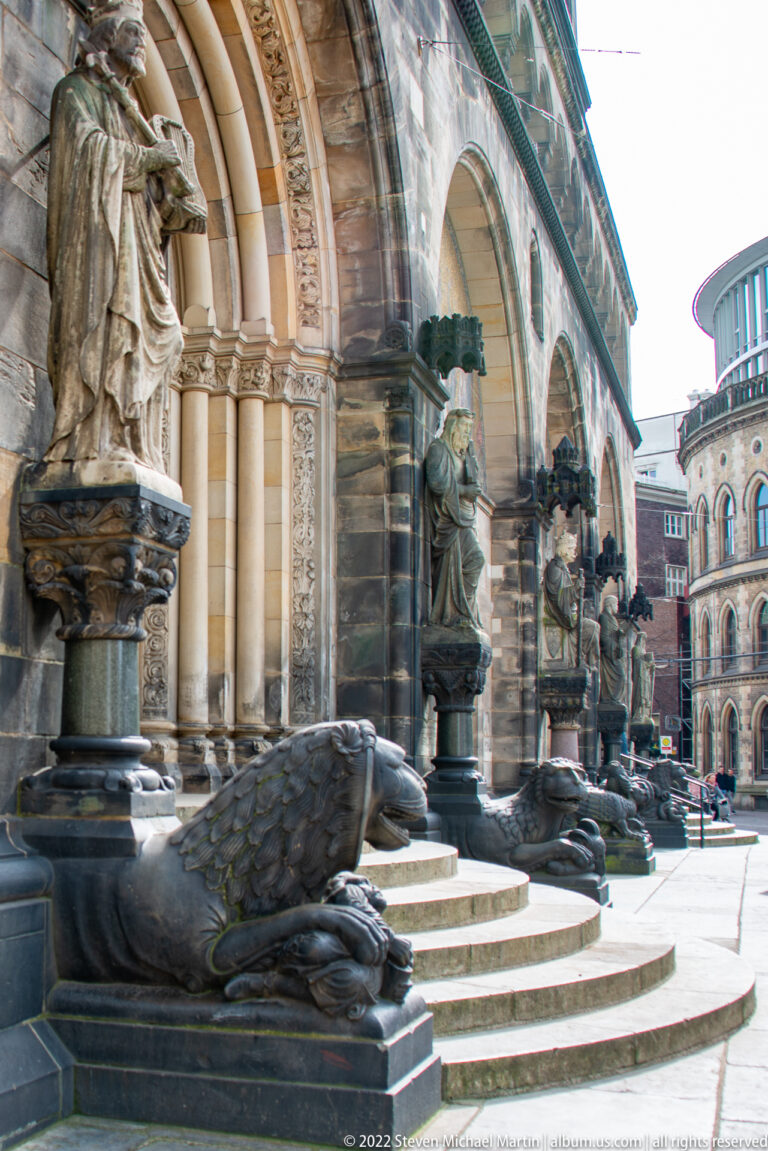 Reclining dark stone animal sculptures lining the steps of an ornate arched entrance at Bremen Cathedral.