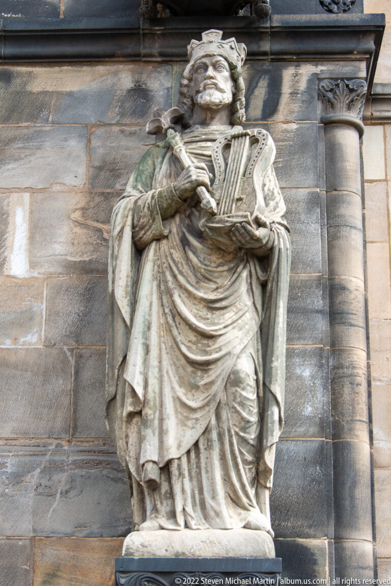 Stone statue of a robed, long-haired figure holding a harp against the exterior wall of Bremen Cathedral.