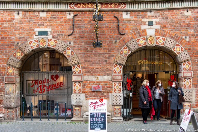 Two decorated arched openings in the brick ground floor of Bremen’s Stadtwaage, with modern shop and venue signage.