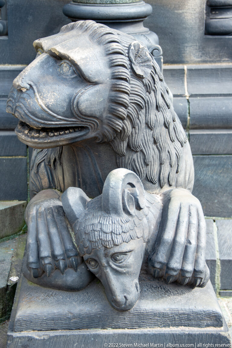 Close-up of a carved stone lion bending over a smaller creature held between its front paws.