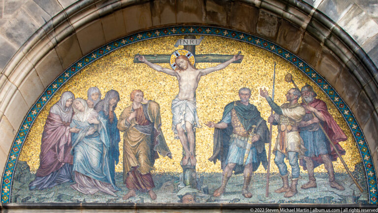 Gold-ground arched mosaic of the Crucifixion with Christ centered between groups of standing figures.