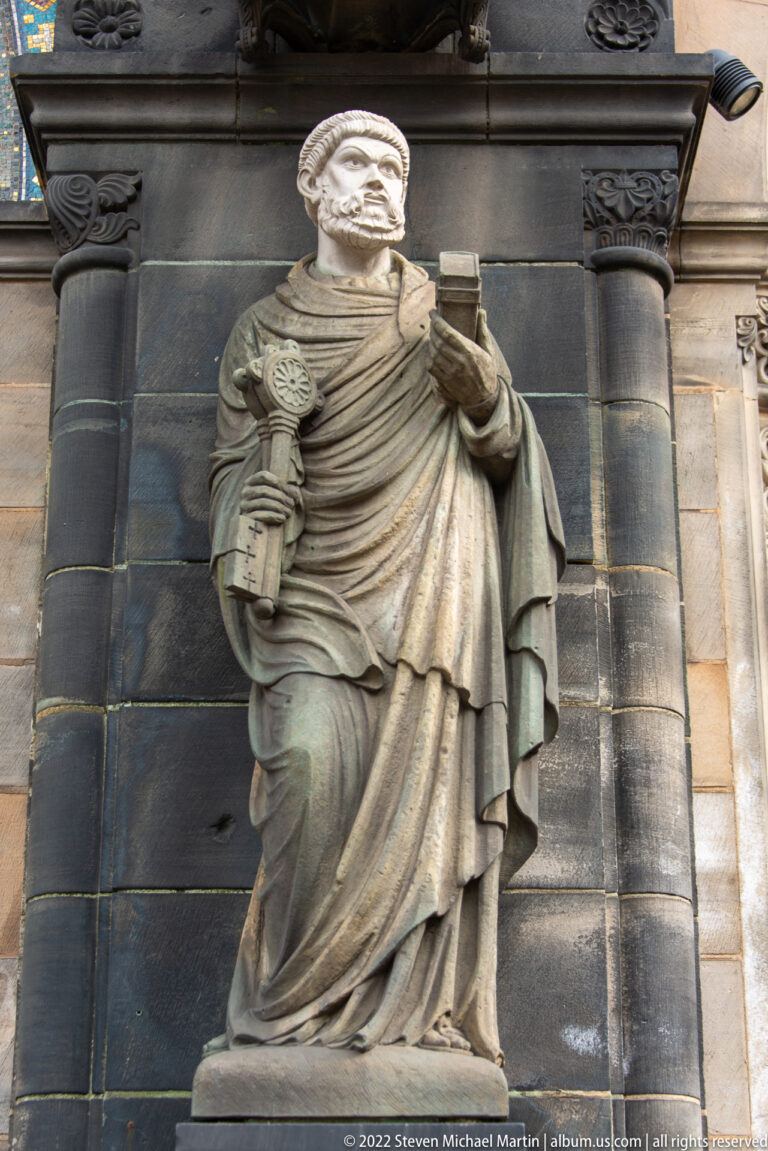 Standing bearded stone figure in robes holding a closed book against the exterior wall of Bremen Cathedral.