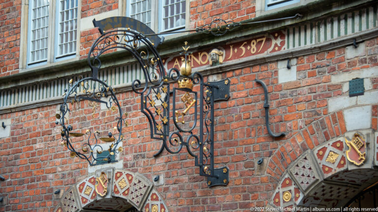 Ornate wrought-iron sign bracket with gilded details mounted on the red-brick façade of Bremen’s Stadtwaage.