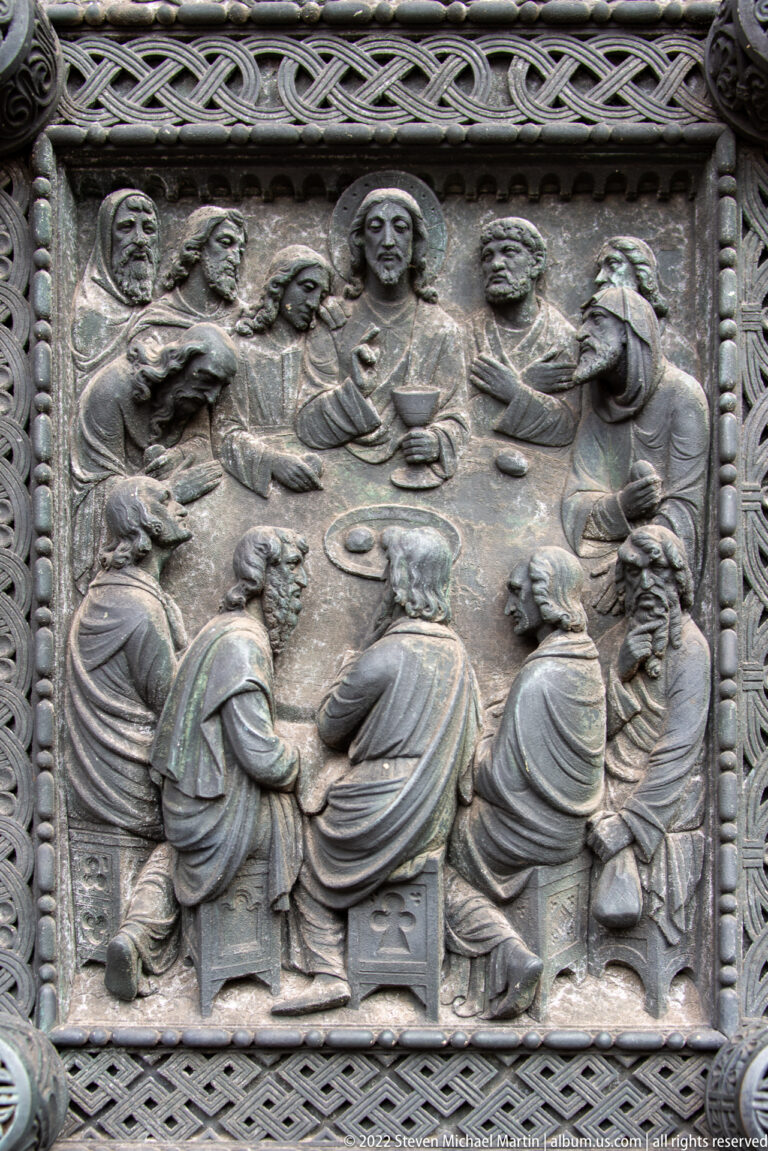 Bronze relief of Christ and the apostles seated around a table in a Last Supper scene.