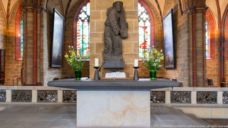 Stone altar with candles and flowers before a tall carved saint in a side chapel of Bremen Cathedral.