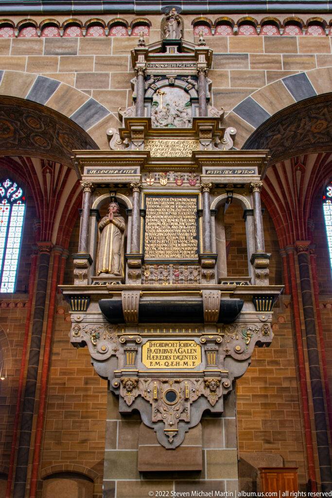 Large ornate wall memorial with columns, sculpted figures, gilded details, and dense inscription panels inside Bremen Cathedral.