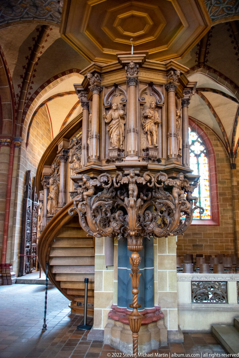 Highly carved wooden pulpit with curved staircase, sculpted figures, columns, and polygonal sounding board inside Bremen Cathedral.