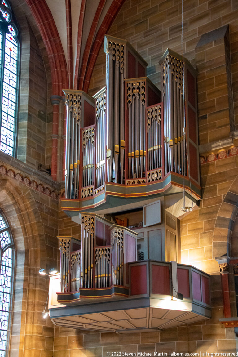 Modern wall-mounted pipe organ with grouped metal pipes and red, green, and gray casework inside Bremen Cathedral.