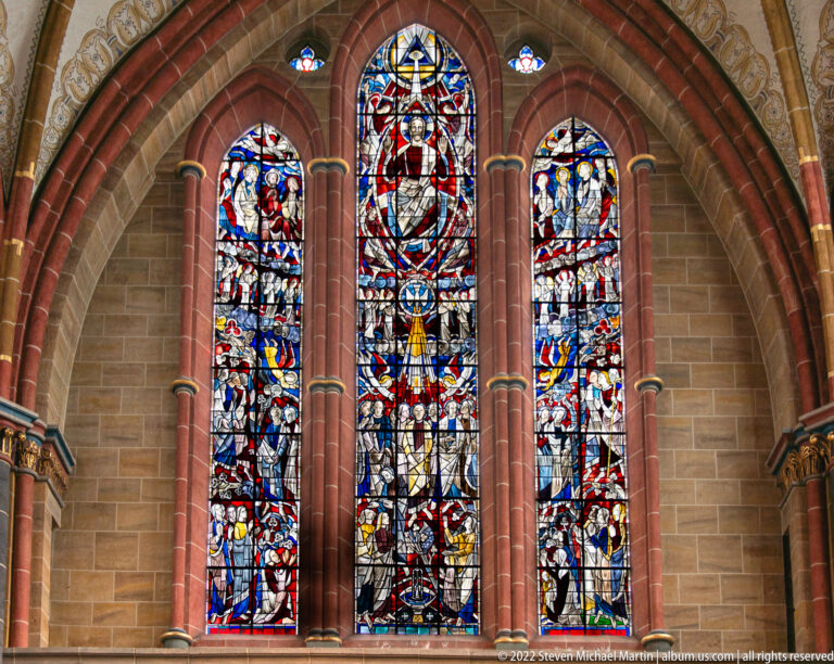 Three tall multicolored stained-glass windows beneath pointed arches, filled with figures and narrative scenes.
