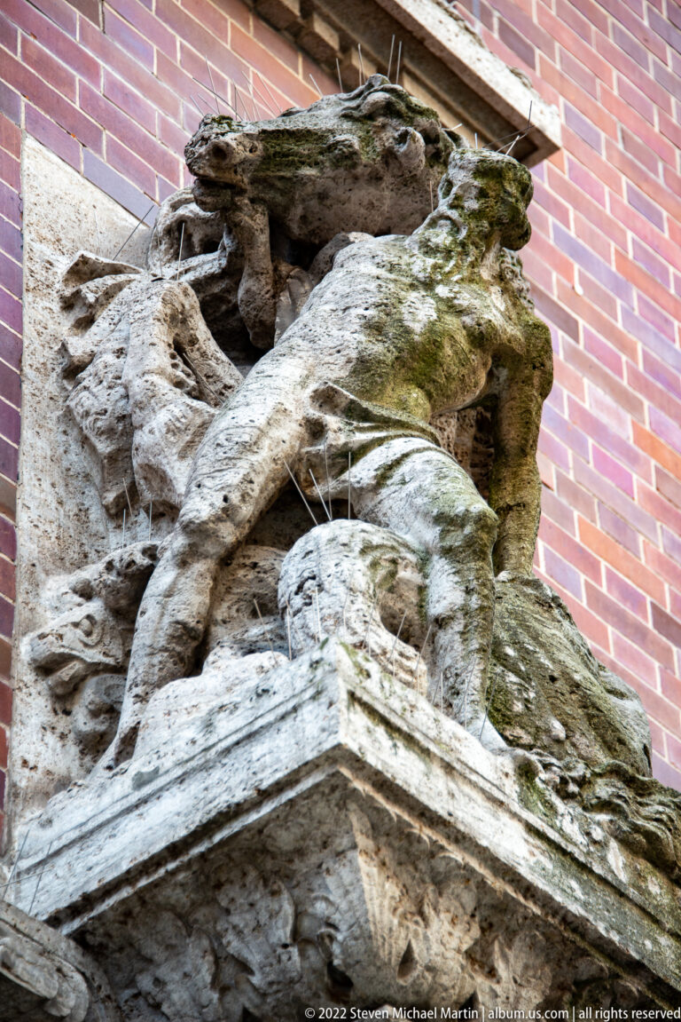 Close view of an eroded projecting stone carving set against a red-brick wall.