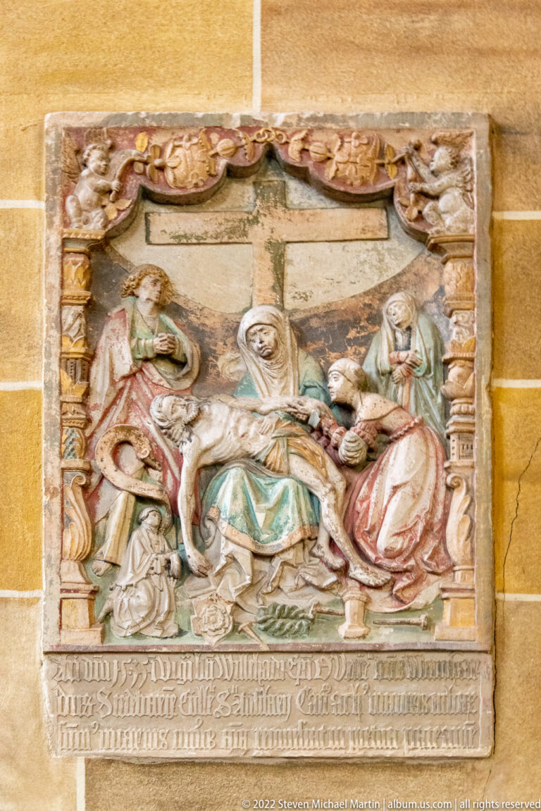 Painted stone relief with robed seated and kneeling figures above a long carved inscription.