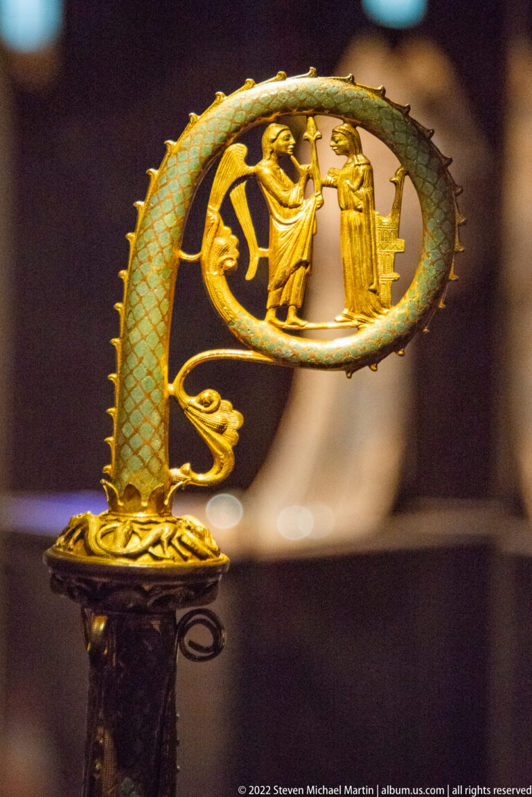 Ornate gilded and turquoise-green dragon-form liturgical staff head with two small standing figures in its central opening.
