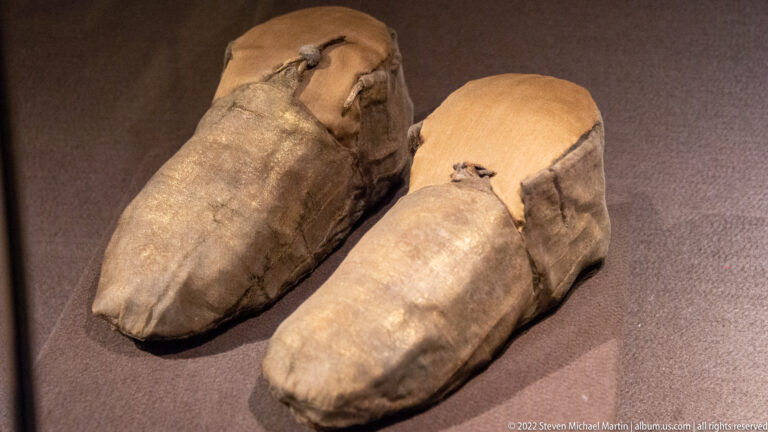Pair of aged leather shoes with rounded toes displayed side by side in a museum case.