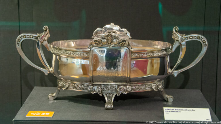 Ornate silver two-handled bowl with decorative rim, cartouche, and four small feet.