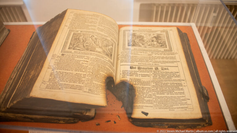 Open old book with blackletter German text and rectangular religious illustrations displayed in a museum case.