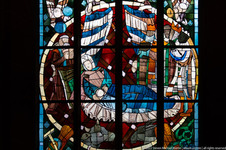 Multicolored stained-glass window with a reclining central figure surrounded by standing attendants.