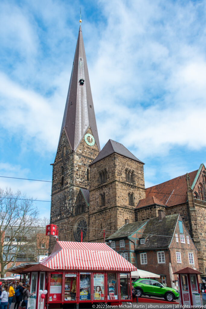 Stone Church of Our Lady in Bremen with steep tower roof, clock, and a striped market stall in the foreground.