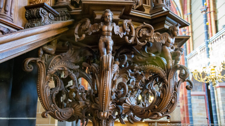 Two carved putti amid dense scrolling foliage and ornamental openwork on a wooden church furnishing.