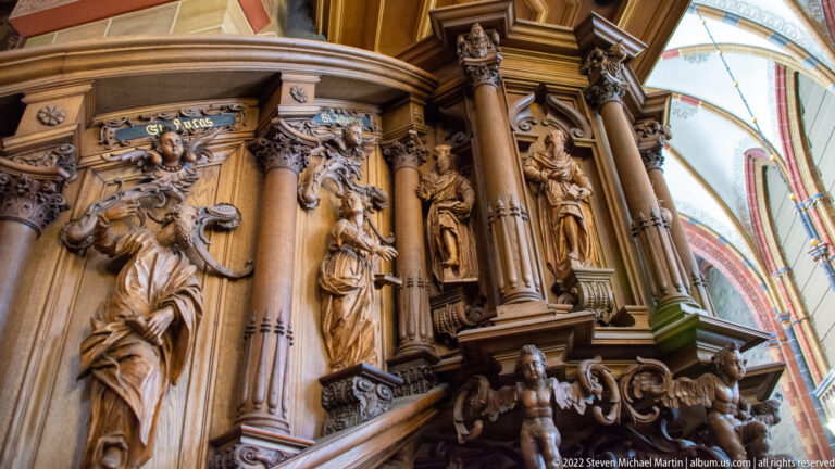 Several standing carved figures in niches between columns on ornate wooden choir stalls.