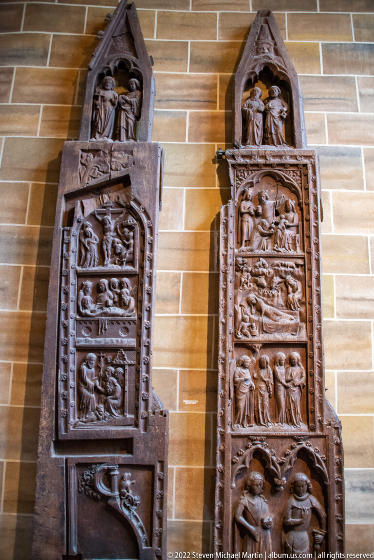 Two tall carved wooden panels with stacked figurative scenes and pointed Gothic canopies.