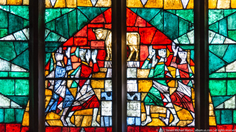 Modern stained-glass panel with several robed figures set among angular fields of bright color.