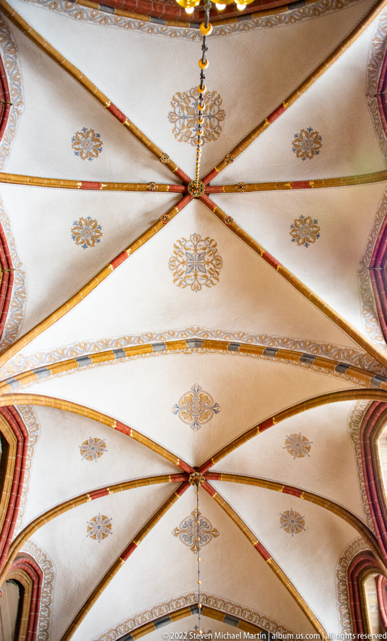 Light-colored ribbed vault with red-and-gold ribs and small gilded floral motifs.