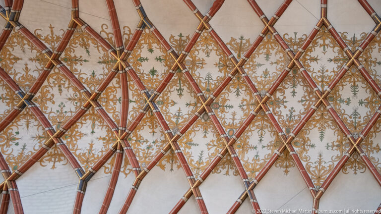 Close view of intersecting red ribs forming diamonds over pale vault fields filled with gold and green ornament.